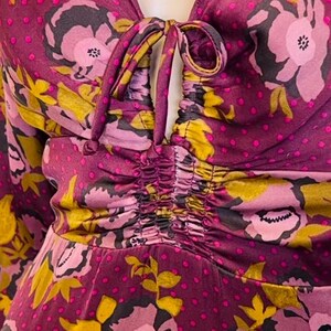 May include: A close-up of a purple and pink floral print dress with a gathered bodice and a tie at the neckline.