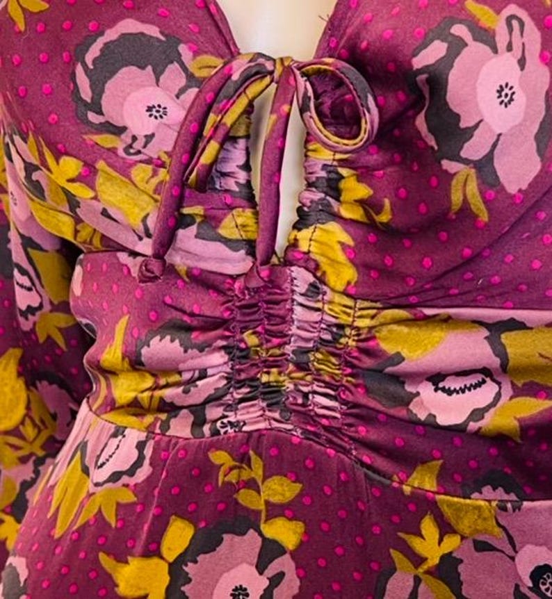 May include: A close-up of a purple and pink floral print dress with a gathered bodice and a tie at the neckline.