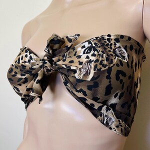 Pode incluir: Um top de tecido estampado de leopardo marrom e preto com um nó na frente. O top é sem alças e tem um caimento solto.