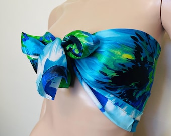 May include: A blue, green, and white patterned silk scarf tied around a mannequin's neck. The scarf has a flowing, abstract design.