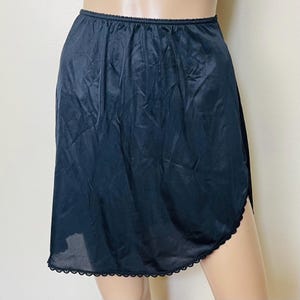 May include: A black half slip with a scalloped lace trim along the hemline. The slip is made of a smooth, shiny fabric and has an elastic waistband. The garment is knee-length and has a slit on one side.