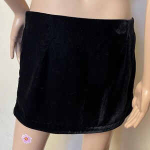 May include: A black velvet mini skirt with a simple design. The skirt is made of a soft, smooth fabric and has a straight silhouette.