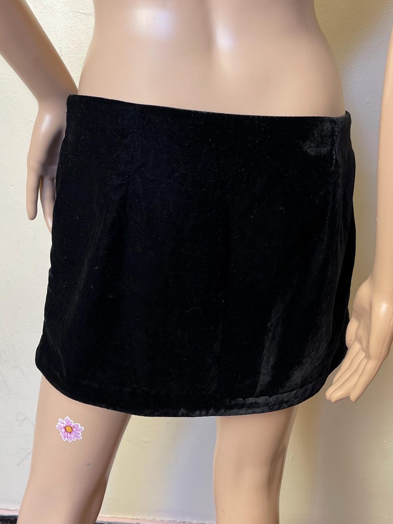 May include: A black velvet mini skirt with a simple design. The skirt is made of a soft, smooth fabric and has a straight silhouette.