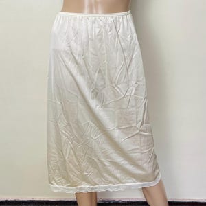 May include: A white half slip with an elastic waistband and a lace trim at the hem. The slip is made of a smooth, lightweight fabric. The garment is designed to be worn under a skirt or dress.