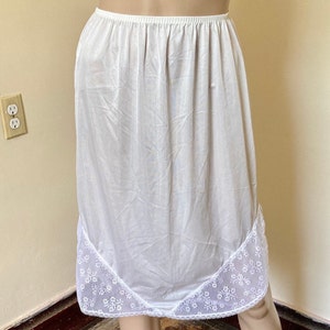 May include: White slip skirt with a lace trim. The skirt is made of a smooth, silky fabric and has a simple, classic design.