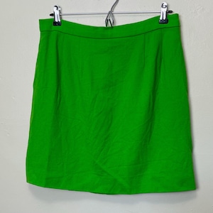 May include: A bright green skirt hanging on a metal hanger. The skirt is a solid color and appears to be made of a woven fabric. The skirt is a mini skirt style.