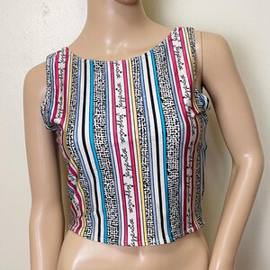May include: A sleeveless crop top with a vertical striped pattern in white, black, pink, blue, and yellow. The top features the word "Jappercise" in a script font. The top is made of a lightweight material.