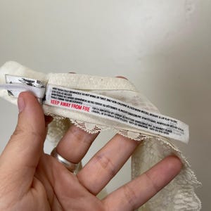 Pu&ograve; includere: Intimo in pizzo bianco sporco con un delicato bordo smerlato. Un'etichetta con istruzioni per la cura e la scritta "KEEP AWAY FROM FIRE" &egrave; visibile. L'indumento &egrave; realizzato in un materiale morbido e leggero.