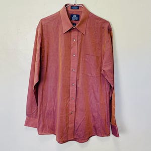 Op de afbeelding: Een roodbruin overhemd met lange mouwen, knoopsluiting en een borstzak. Het overhemd heeft een klassieke kraag en het label "Stafford". Het hangt aan een metalen hanger. De kleur is warm.