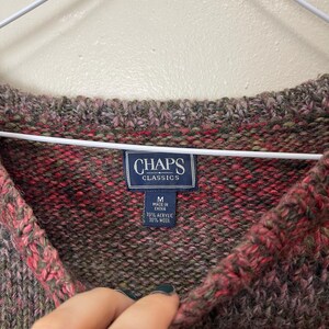 May include: A close-up of a multi-colored sweater with a V-neck. The sweater is a blend of red, green, and brown hues. The label reads "CHAPS CLASSICS" and indicates the sweater is size M, made in China, with 70% acrylic and 30% wool.