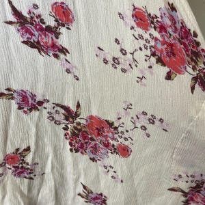 Op de afbeelding: Cr&egrave;mekleurige stof met een getextureerd oppervlak, versierd met een bloemenpatroon. De bloemen zijn rood, roze en paars, met groene bladeren. Het ontwerp is verspreid over de stof.