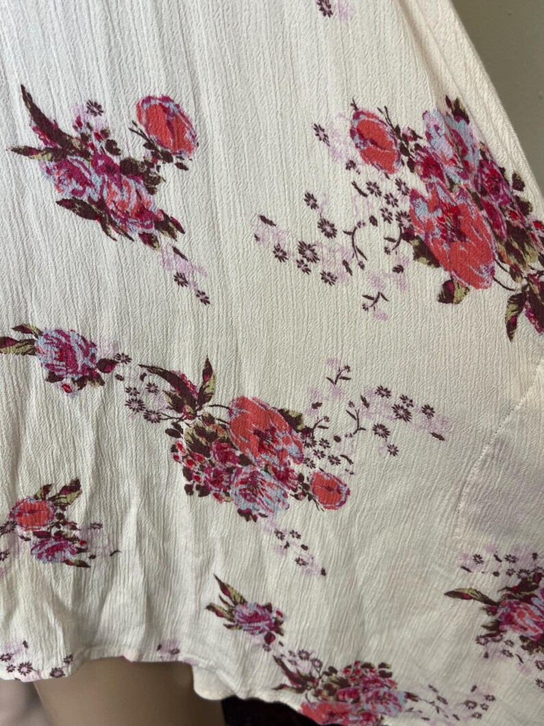 Op de afbeelding: Cr&egrave;mekleurige stof met een getextureerd oppervlak, versierd met een bloemenpatroon. De bloemen zijn rood, roze en paars, met groene bladeren. Het ontwerp is verspreid over de stof.