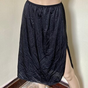 May include: Black slip skirt with a side slit and lace trim. The skirt is made of a silky material and is knee-length.