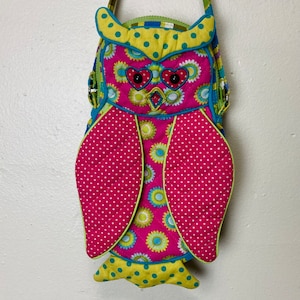 Puede incluir: Un bolso de hombro en forma de búho rosa y verde con un patrón de lunares y ojos en forma de corazón.