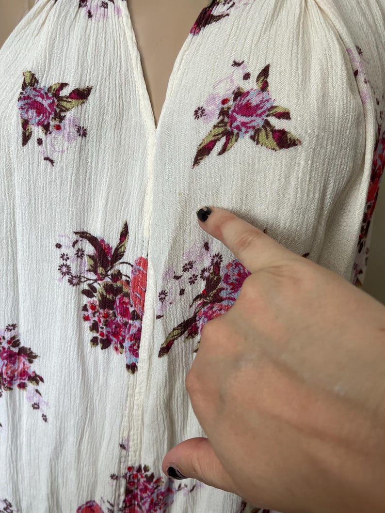 Op de afbeelding: Cr&egrave;mekleurige top met een V-hals en een bloemenpatroon in roze, rode en groene tinten. De stof heeft een getextureerde uitstraling. De afbeelding toont een close-up van de top.