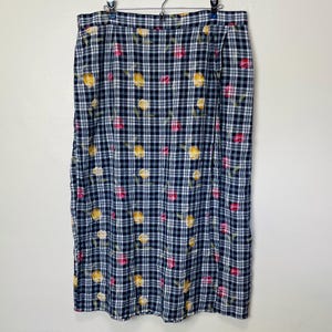 May include: A navy blue and white plaid skirt with a floral pattern of yellow and pink flowers. The skirt is hanging on a hanger against a white background. The skirt is a midi length.