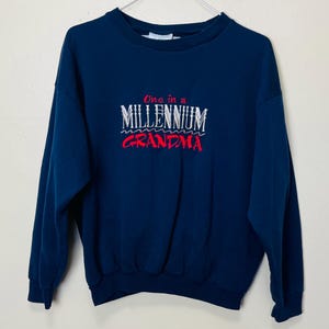 May include: A navy blue sweatshirt with the text "One in a Millennium Grandma" embroidered on the front in white and red.
