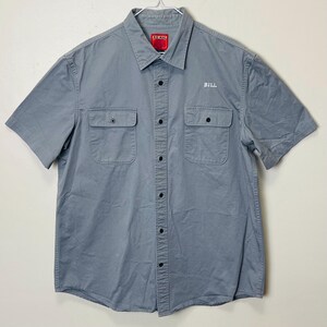 May include: A gray short-sleeved button-down shirt with two chest pockets and the name "BILL" embroidered on the right side. The shirt has a collar and is labeled "BIG MAC" on the neck tag.