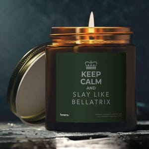 Peut inclure: Une bougie allumée dans un bocal en verre avec un couvercle doré. L'étiquette sur le bocal est vert foncé avec le texte "KEEP CALM AND SLAY LIKE BELLATRIX" en blanc. Le bocal est ouvert et le couvercle est posé à côté.