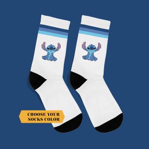 May include: Pair of white socks featuring a blue cartoon character with large ears. The socks have a black heel and toe, and blue stripes at the top. The text "CHOOSE YOUR SOCKS COLOR" is on a yellow banner.