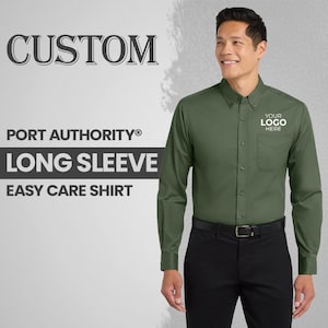 May include: A long-sleeve, easy-care shirt in a dark green color. The shirt has a button-down collar, a chest pocket, and the text "YOUR LOGO HERE" printed on the pocket. The text "CUSTOM", "PORT AUTHORITY® LONG SLEEVE EASY CARE SHIRT" is also visible.