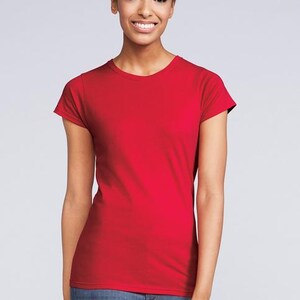 Pu&ograve; includere: Una maglietta rossa tinta unita con scollo tondo e maniche corte. La maglietta &egrave; indossata con jeans blu. Lo sfondo &egrave; di colore grigio chiaro.