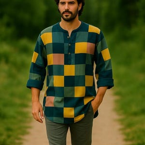 Puede incluir: Una camisa de manga larga con un estampado a cuadros en tonos verde, amarillo y rosa. La camisa tiene cuello Henley y se combina con pantalones grises. La persona camina por un camino de tierra. El diseño de la camisa recuerda a un patchwork.