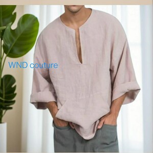 May include: A light pink linen shirt with a wide neckline and three-quarter sleeves. The shirt has a front pocket and the text "WND couture" is visible on the left side. The model is wearing gray pants.