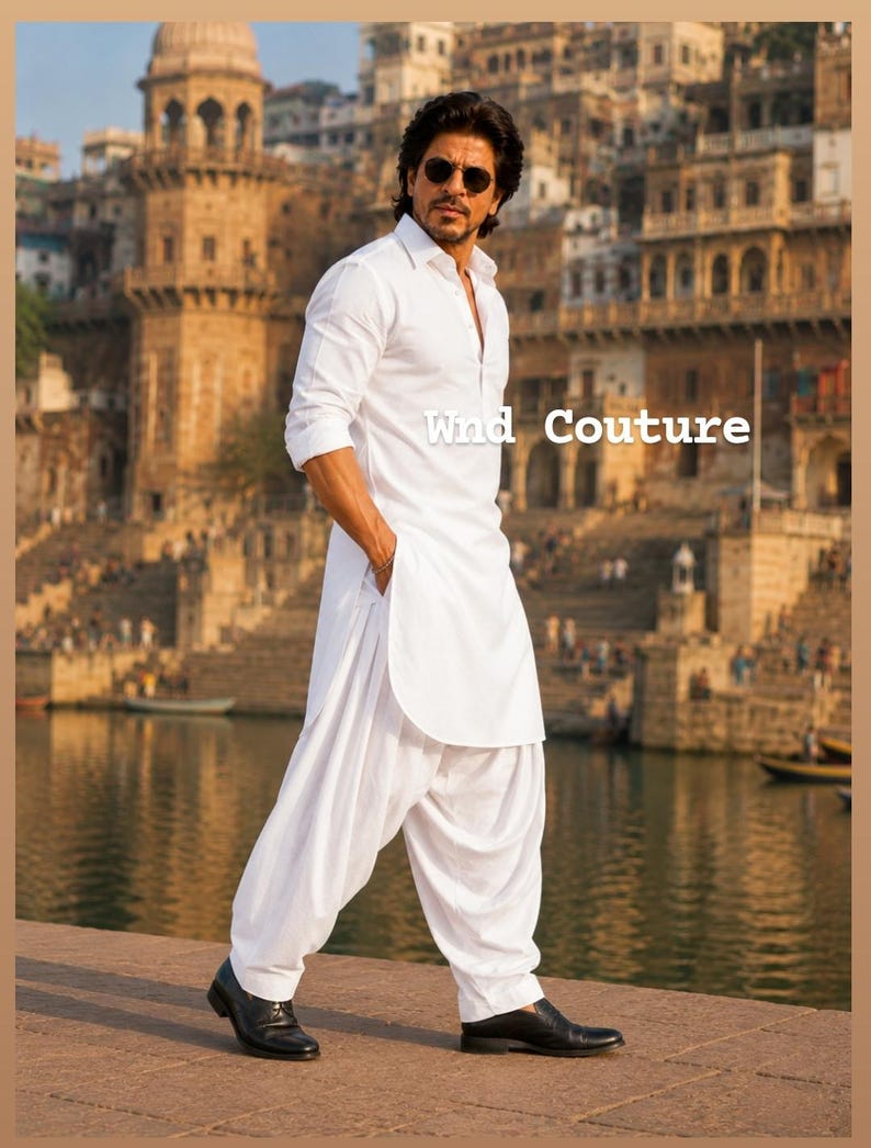 May include: A man wearing a white kurta and salwar suit, with black shoes, stands on a stone surface. The text "Wind Couture" is visible. The background features a body of water and buildings.