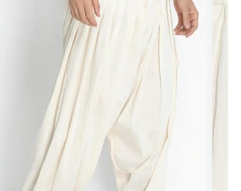 May include: Off-white, loose-fitting pants with a gathered waist and a relaxed, draped design. The pants are made of a lightweight fabric and are paired with black shoes. The overall style suggests comfort and casual wear.