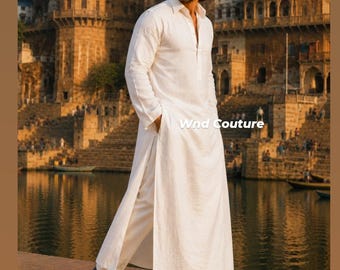 May include: A white long-sleeved kurta with a collar and side slits, paired with matching white trousers and black shoes. The garment features the text Wnd Couture in white lettering. The attire is worn by a person with dark hair and sunglasses.
