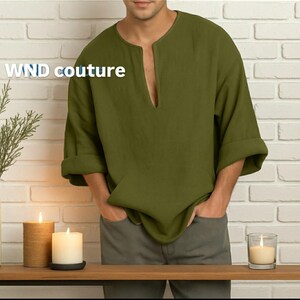 May include: Olive green linen shirt with a V-neck and rolled-up sleeves. The shirt has a relaxed fit and is paired with gray pants. The text "WND couture" is printed on the shirt. The background includes candles and a brick wall.