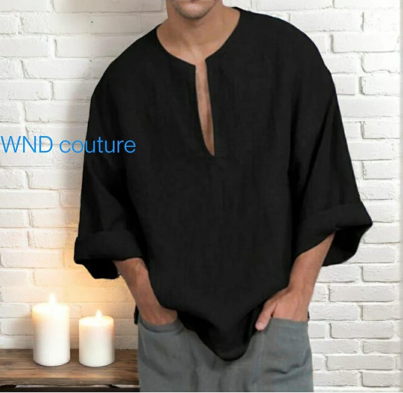 May include: Black long-sleeve shirt with a deep V-neck. The shirt has rolled-up sleeves and is made of a textured fabric. The text "WND couture" is visible on the left side of the shirt. The shirt is paired with gray pants.
