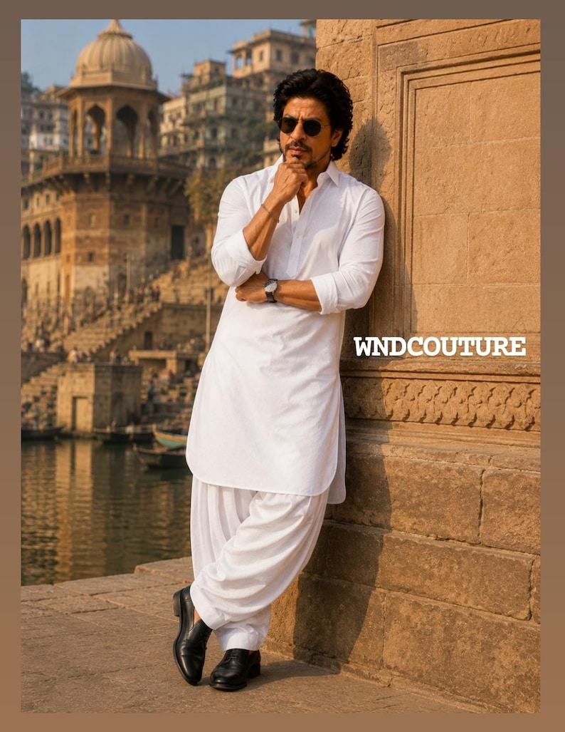 May include: A man in a white kurta pajama, leaning against a stone wall. He wears black shoes and a watch. The image includes the text "WNDCOUTURE". The background features a cityscape with a river and buildings.