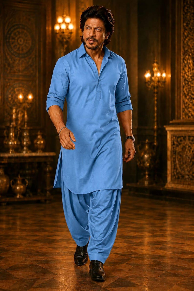 May include: A man in a light blue kurta pajama, a traditional South Asian outfit, walks forward. The outfit includes a collared shirt and loose-fitting pants. He wears black dress shoes and a watch. The background features ornate decor and warm lighting.