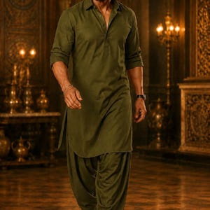 May include: A man in an olive green kurta and salwar suit walks forward. The traditional Indian outfit includes a long-sleeved shirt and loose-fitting pants. He wears black dress shoes and a watch. The background features ornate decor and warm lighting.