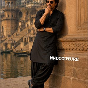 May include: A man in a black kurta and salwar suit, leaning against a stone wall. He wears sunglasses and a wristwatch. The text "WNDCOUTURE" is visible. The background features a river and buildings.