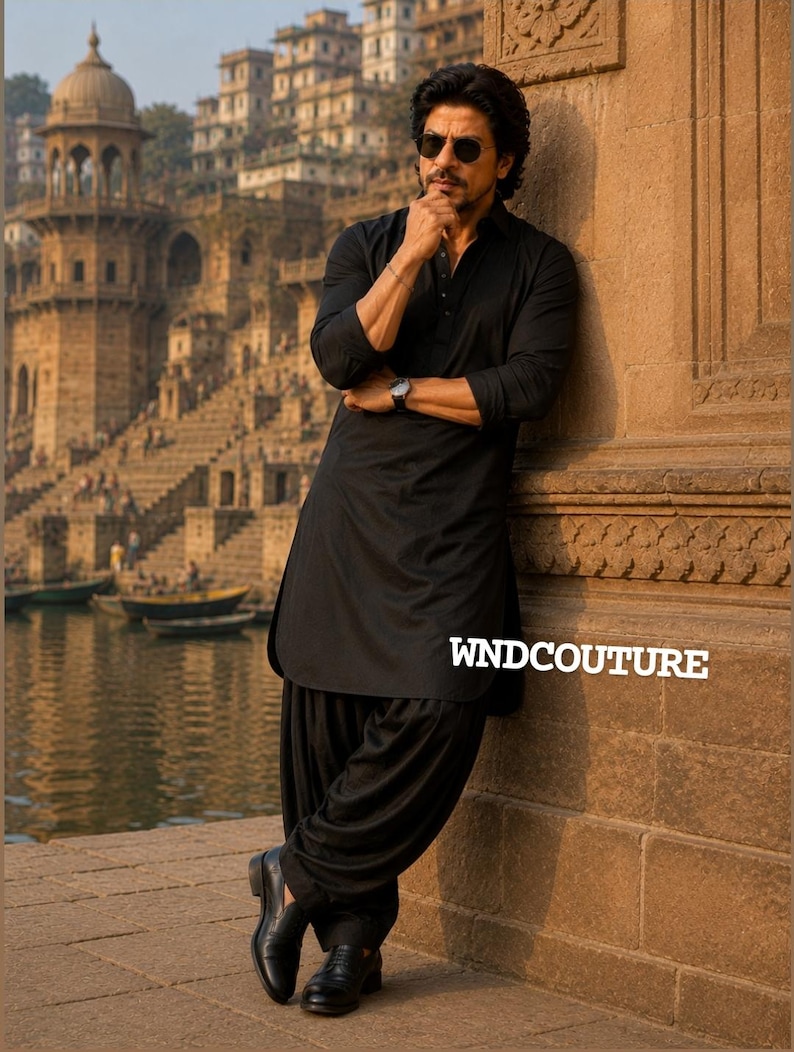 May include: A man in a black kurta and salwar suit, leaning against a stone wall. He wears sunglasses and a wristwatch. The text "WNDCOUTURE" is visible. The background features a river and buildings.