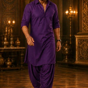 May include: A man in a purple kurta pajama, a traditional South Asian outfit, walks forward. The long-sleeved shirt is buttoned at the collar. The pants are loose and gathered at the ankles. He wears black dress shoes. The background is a room with ornate decor.