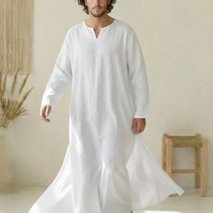 May include: A white linen robe with long sleeves and a V-neck. The robe is floor-length and has a flowing design. The image shows a person wearing the robe. The background is a neutral color.