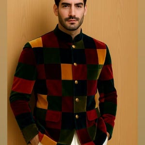 May include: A multi-coloured chequered jacket with a mandarin collar and gold buttons. The jacket features a patchwork design in shades of red, green, yellow, and black. The person is wearing white trousers.