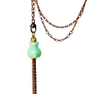 May include: A delicate green glass vase pendant necklace with a floral design and a copper chain.