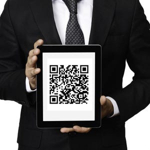 May include: A person in a black suit holds a tablet displaying a black and white QR code.