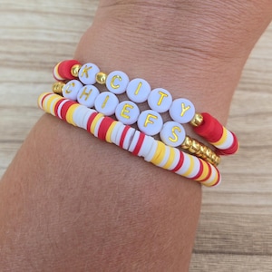 Könnte beinhalten: Drei Armbänder aus roten, weißen und gelben Perlen. Ein Armband schreibt "K CITY CHIEFS" in goldenen Buchstaben auf weißen Perlen. Die anderen Armbänder haben eine Mischung aus roten, weißen und gelben Scheibenperlen. Die Armbänder werden an einem Handgelenk getragen.