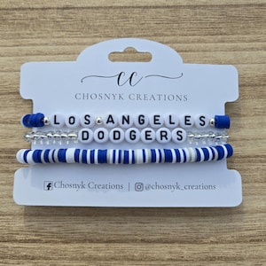 May include: Three bracelets on a white card. The top bracelet spells "LOS ANGELES" with white letter beads. The middle bracelet has silver beads. The bottom bracelet is blue, white, and silver. The card has the text "CHOSNYK CREATIONS".