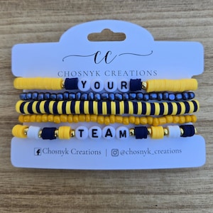 May include: A set of five beaded bracelets on a white display card labeled Chosnyk Creations. The bracelets feature yellow, navy blue, and metallic beads, with white letter beads spelling out the phrase YOUR TEAM across two strands.