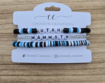 May include: Three beaded bracelets on a white card. The top bracelet spells "UTAH" with white letter beads. The middle bracelet is clear beads. The bottom bracelet spells "MAMMOTH" with white letter beads. The card has the text "Chosnyk Creations".
