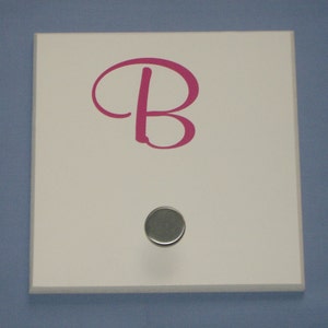 May include: White wooden sign with a pink letter "B" and a silver hook.