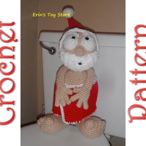 May include: Crocheted Santa Claus doll wearing a red and white Santa hat and a red crocheted skirt. The doll is sitting on a white toilet seat. The text "Erin's Toy Store" is visible in the background.