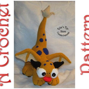 Pode incluir: Um dragão amarelo de crochê com manchas azuis, chifres pretos e grandes olhos brancos. O dragão tem uma cauda longa e asas. O dragão está sentado em um fundo branco. Erin's Toy Store Crochet Patterns.